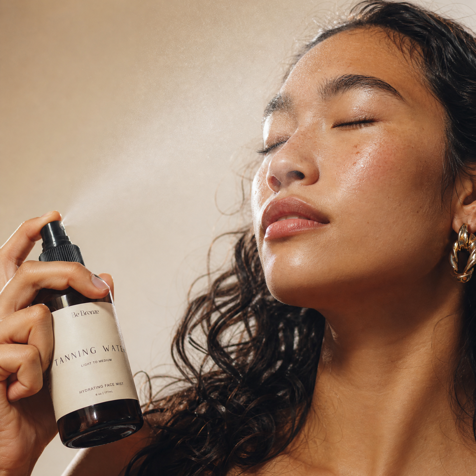 Woman holding a tanning face mist with a neutral background